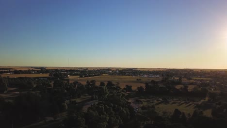 Vista-Aérea-De-Drones-Subiendo-En-Un-Pequeño-Pueblo-Agrícola-Durante-La-Puesta-De-Sol,-En-Coronel-Dorrego,-Argentina