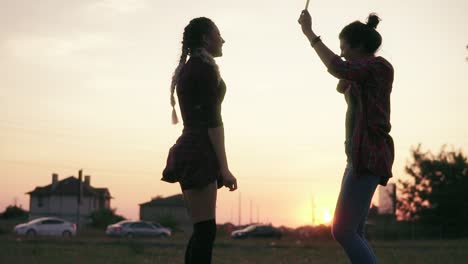 Two-Attractive-Girlfriends-Dancing-Together-And-Waving-With-Firework-Candles-During-Sunset