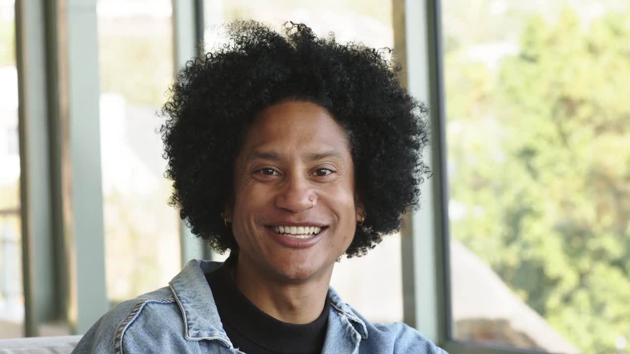 African American man gazing out window in lounge turning head lowering hand smiling to greet viewer