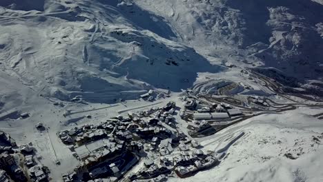 view of val thorens frozen grounds surrounded by snow-capped mountain range - aerial pan tilt-up shot