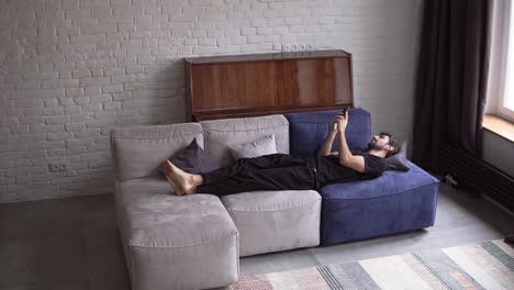 Man-lying-on-couch-using-smartphone,-scrolling-various-gestures-like-swiping-and-scrolling