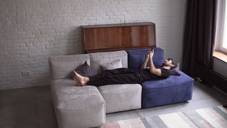 man lying on couch using smartphone, scrolling various gestures like swiping and scrolling