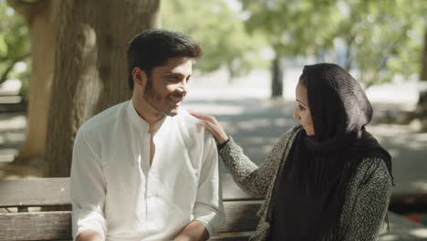 Young-muslim-couple-sitting-on-bench-in-park-on-hot-summer-day.