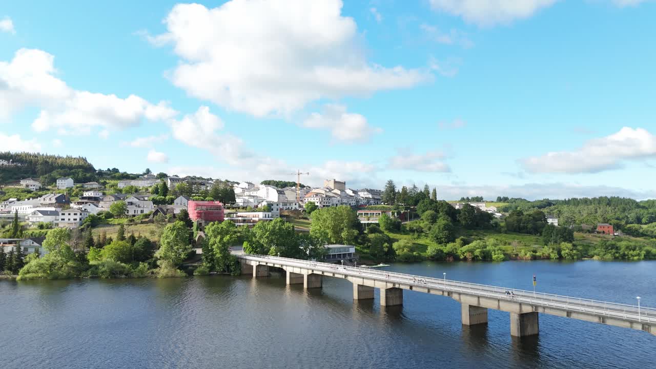 Aerial shot of pilgrims crossing the bridge toward Portomarín on the Camino de Santiago. Scenic travel scene blending human journey, history, architecture and natural landscape in Galicia.
