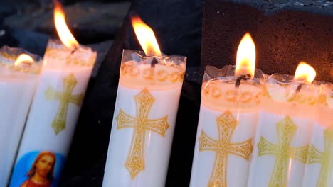 Religious-wax-candles-burning,-flames-flickering-in-breeze,-with-Jesus-Christ-and-cross-symbol-during-church-congregation