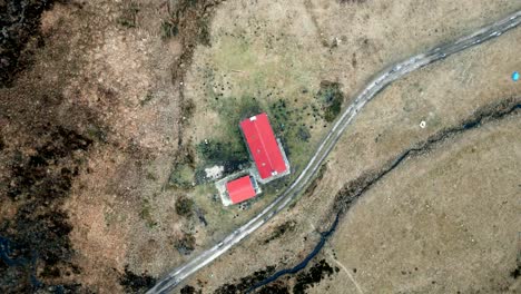 a drone slowly rises above the red roof of a remote bothy in the highlands of scotland in winter