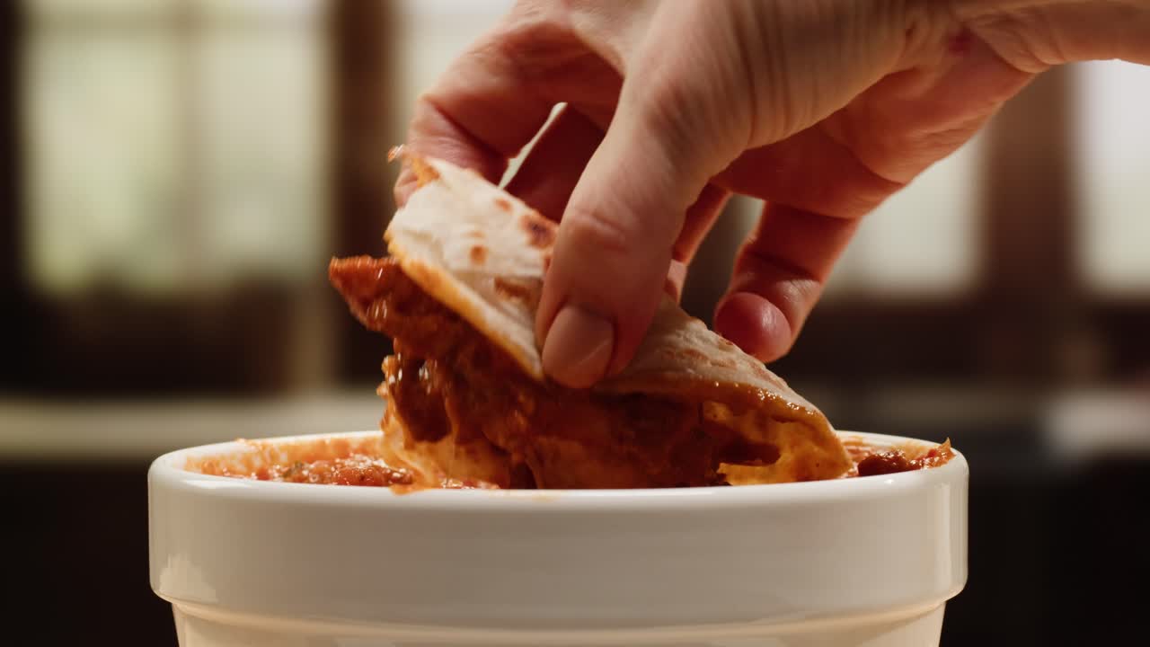 Hand dipping tortilla in sauce
