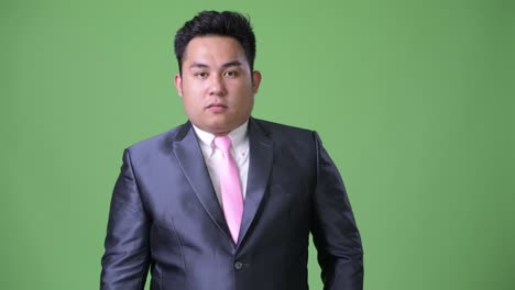 young handsome overweight asian businessman against green background