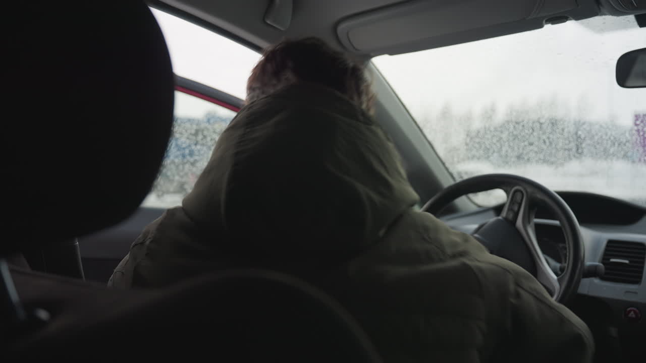Young boy in winter jacket exits car during cold season with water droplets on window, urban background softly blurred through glass in winter environment