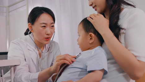 Mother with her cute baby visiting pediatrician, doctor examining little boy with stethoscope in clinic.