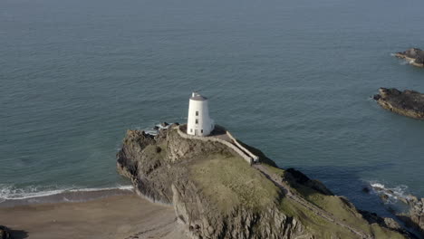 an aerial view of twr mawr lighthouse on ynys llanddwyn island, flying left to right around the lighthouse while elevating and zooming out, anglesey, north wales, uk