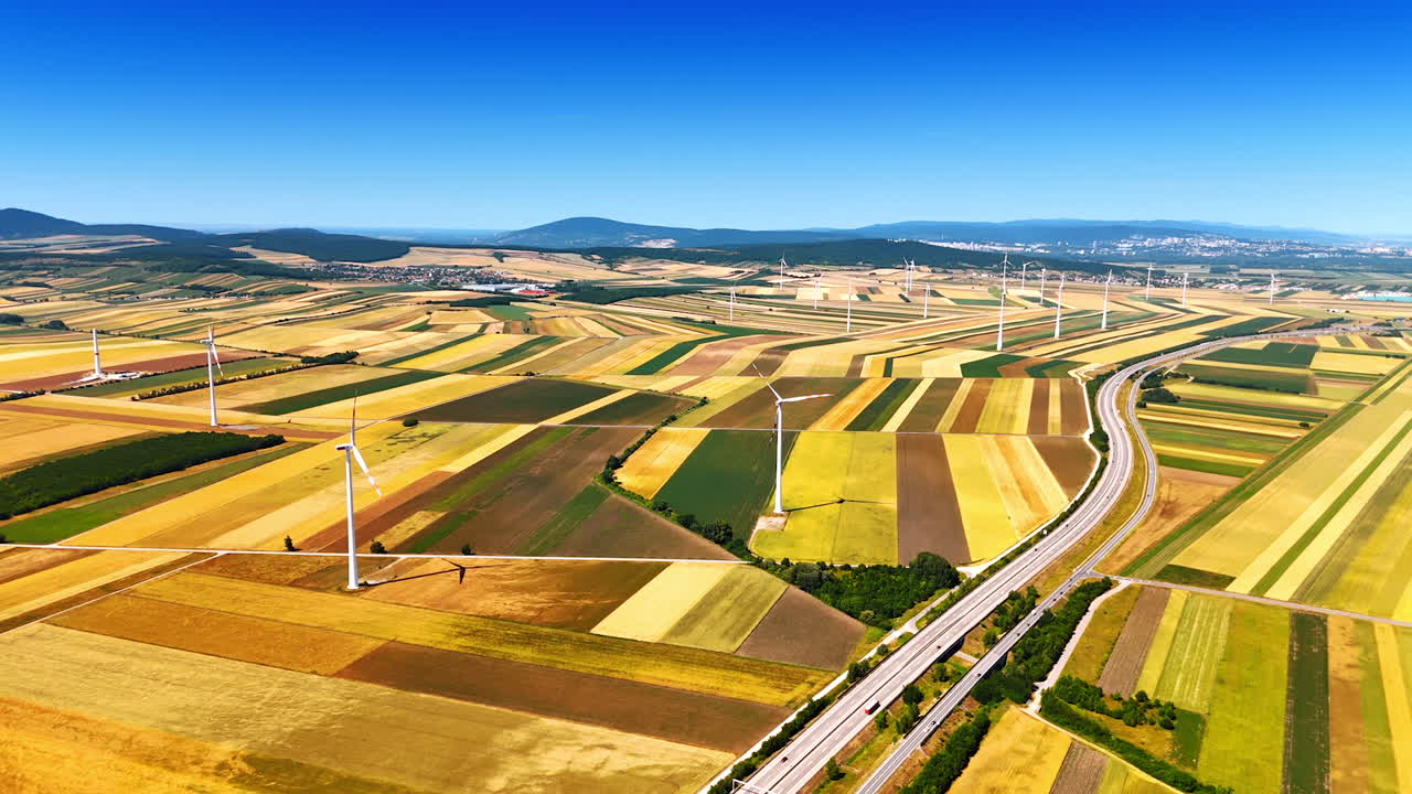 Colorful patched agricultural field crossed by the highways. Wind mills work in the countryside. Aerial view