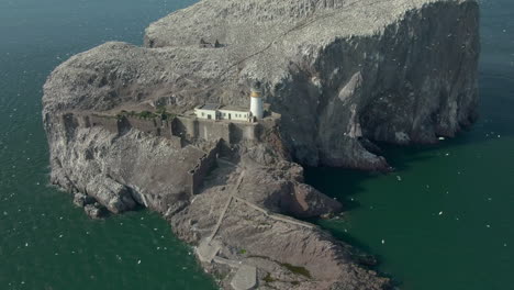 An-aerial-view-circling-Bass-Rock-and-lighthouse-as-gannet-seabirds-circle-their-island-colony-on-a-sunny-day,-East-Lothian,-Scotland