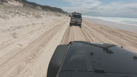 un jeep negro conduciendo sobre la suave arena de la playa siguiendo a otros 4x4 a medida que sube la marea