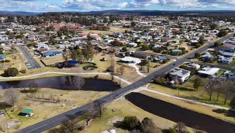 drone footage glides above a quiet suburban neighborhood with houses, parked cars, and intersecting streets under bright daylight and partly cloudy skies