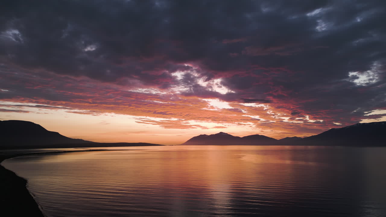 Wonderful drone fly of vivid sunset reflecting over the calm fjord and distant mountains in golden light, Eyjafjordur, Northern Iceland