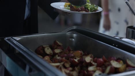hombre poniendo el horno asado patata de piel roja en el plato del buffet de la boda