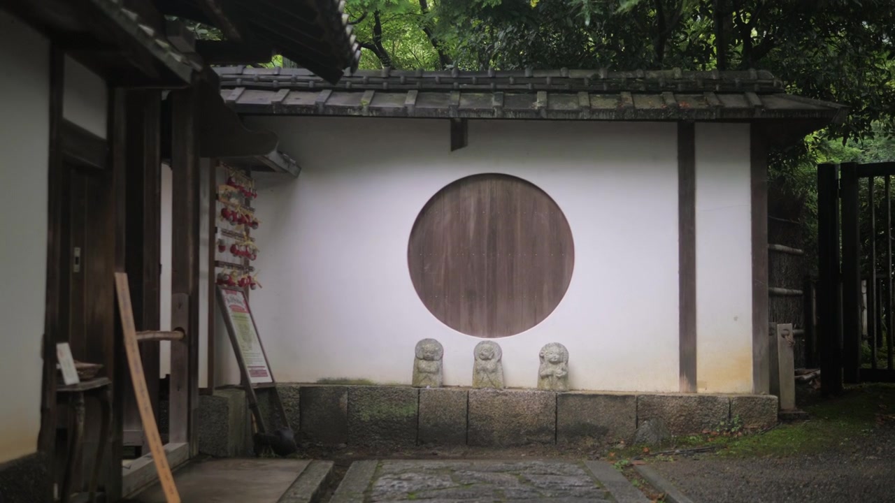 Stensti fører til en traditionel træport med rundt vindue i en Kyoto-have.