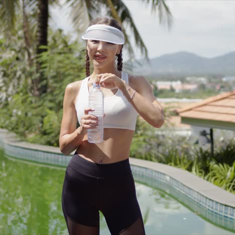 Slim-sportswoman-drinking-water-near-swimming-pool