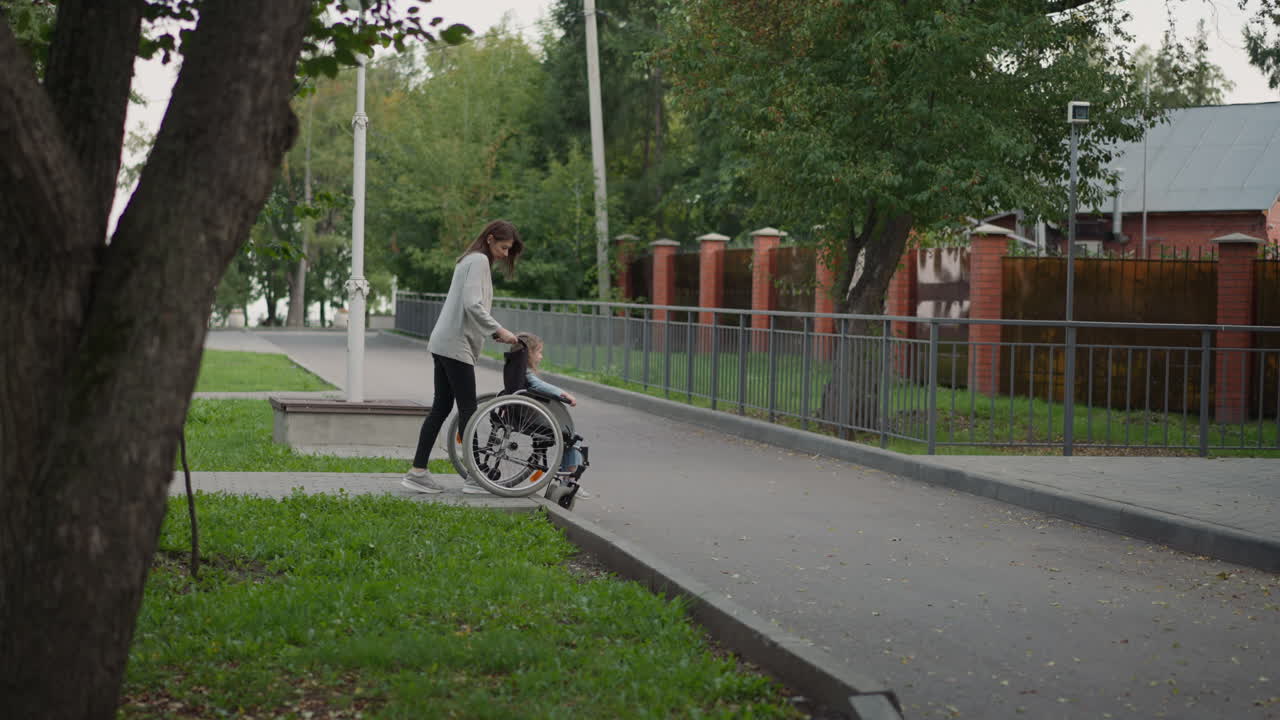 madre baja cuidadosamente la silla de ruedas con la hija en la carretera