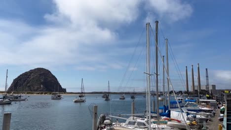 Cinematic-wide-booming-down-shot-of-the-iconic-three-stacks-and-a-rock-from-the-marina-in-Morro-Bay,-California