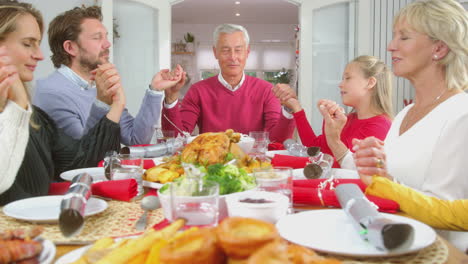 multi generation family hold hands around table at home saying grace before eating christmas meal