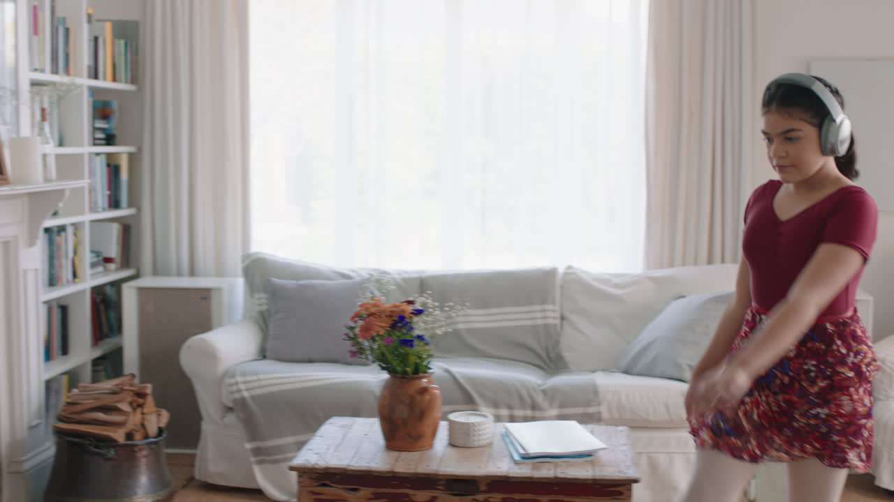 행복한 십대 소녀가 춤을 추고 집에서 발레 춤 동작을 연습하고 음악을 듣고 헤드폰을 착용하고 재미있게 주말을 즐기고 있습니다.