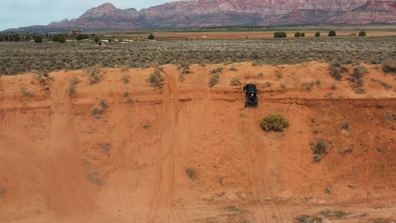 tomada de un avión no tripulado de un vehículo todoterreno subiendo una colina empinada en un paisaje desértico