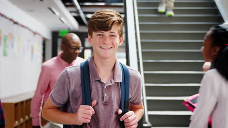 portrait of male high school student standing by stairs in college building