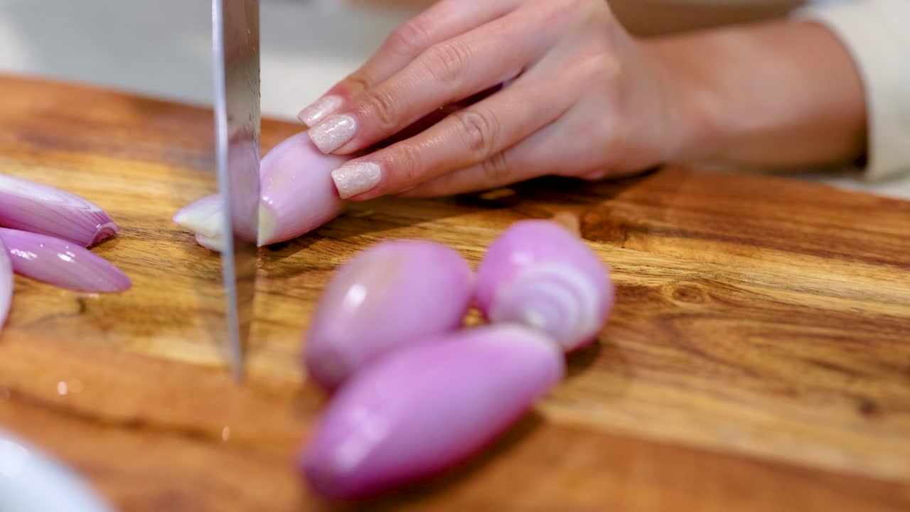 Close-up of hands slicing shallots on a wooden board with natural lighting, showcasing culinary precision and technique