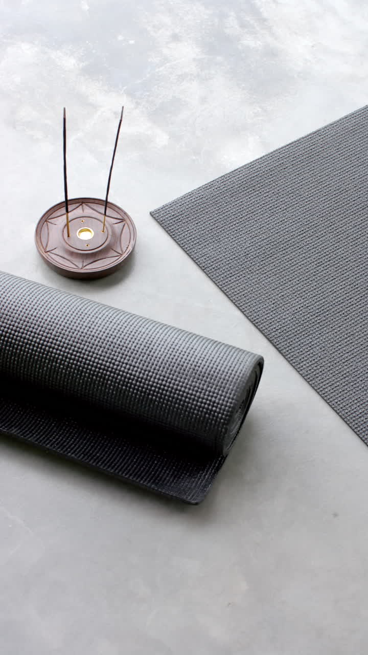 Vertical video: Rolled yoga mat and incense sticks on floor, creating peaceful home atmosphere