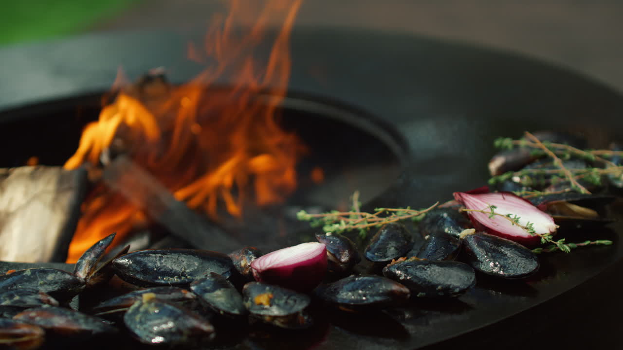 야외에서 양파와 허브로 조개를  ⁇ 는 사람. 해산물을 요리하는 셰프