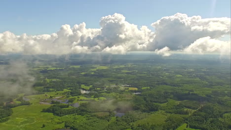 Punto-De-Vista-Aéreo-De-Nubes-Blancas-A-Través-Del-Cielo-Azul-Sobre-Un-Exuberante-Paisaje-Verde