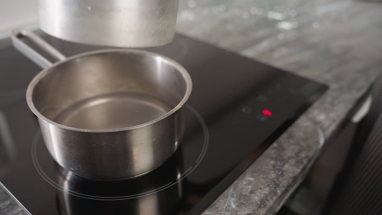 Chef activates touch control on electric stove as pot of water is placed for boiling and preparation begins for double boiling technique with mixing bowl, showcasing modern kitchen setup