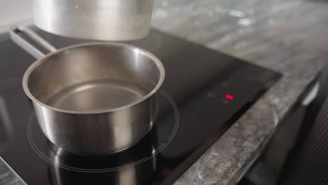 chef activates touch control on electric stove as pot of water is placed for boiling and preparation begins for double boiling technique with mixing bowl, showcasing modern kitchen setup