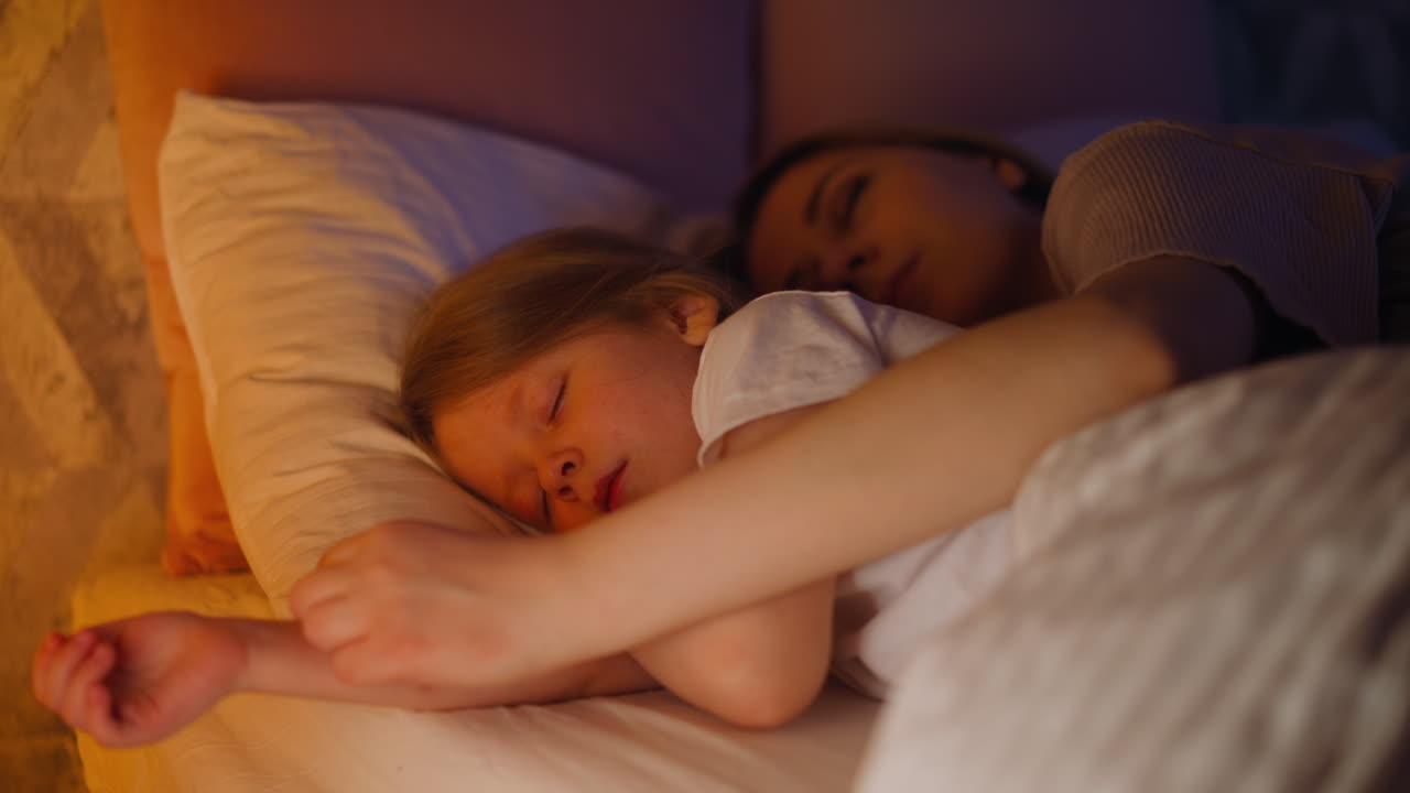 Lady hugs blonde girl sleeping together in comfortable bed