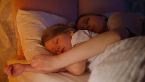 Lady-hugs-blonde-girl-sleeping-together-in-comfortable-bed