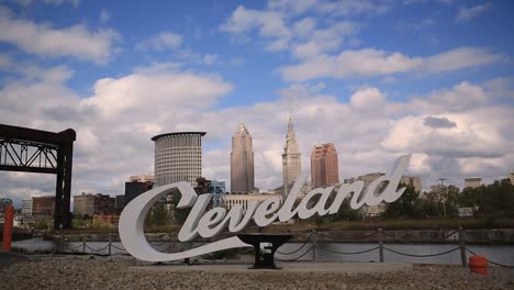 Cleveland,-Ohio-script-sign-on-a-sunny-day-with-clouds-passing-by-a-blue-sky-and-a-cargo-shipping-freighter-passes-by