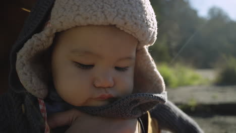 adorable mixed race asian baby wrapped up warm in the outdoors trying to eat an orange fruit