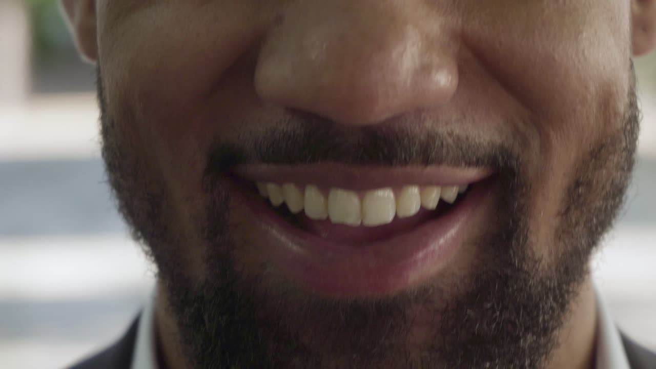 una foto recortada de un hombre con barba y una sonrisa dentada.