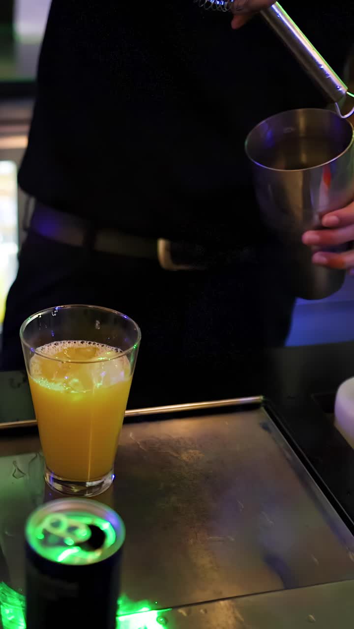 Bartender prepares cocktail with shaker and strainer under colorful bar lighting, close-up perspective