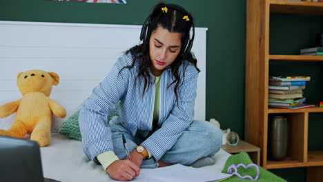 young woman studying in bedroom with laptop and headphones