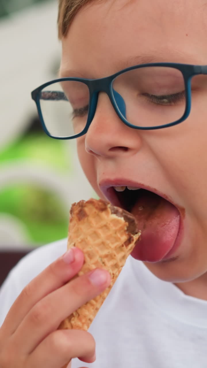 se ve a un niño pequeño disfrutando de su cono de helado, centrándose atentamente en su regalo, con parte de otra persona visible en el lado