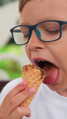 se ve a un niño pequeño disfrutando de su cono de helado, centrándose atentamente en su regalo, con parte de otra persona visible en el lado