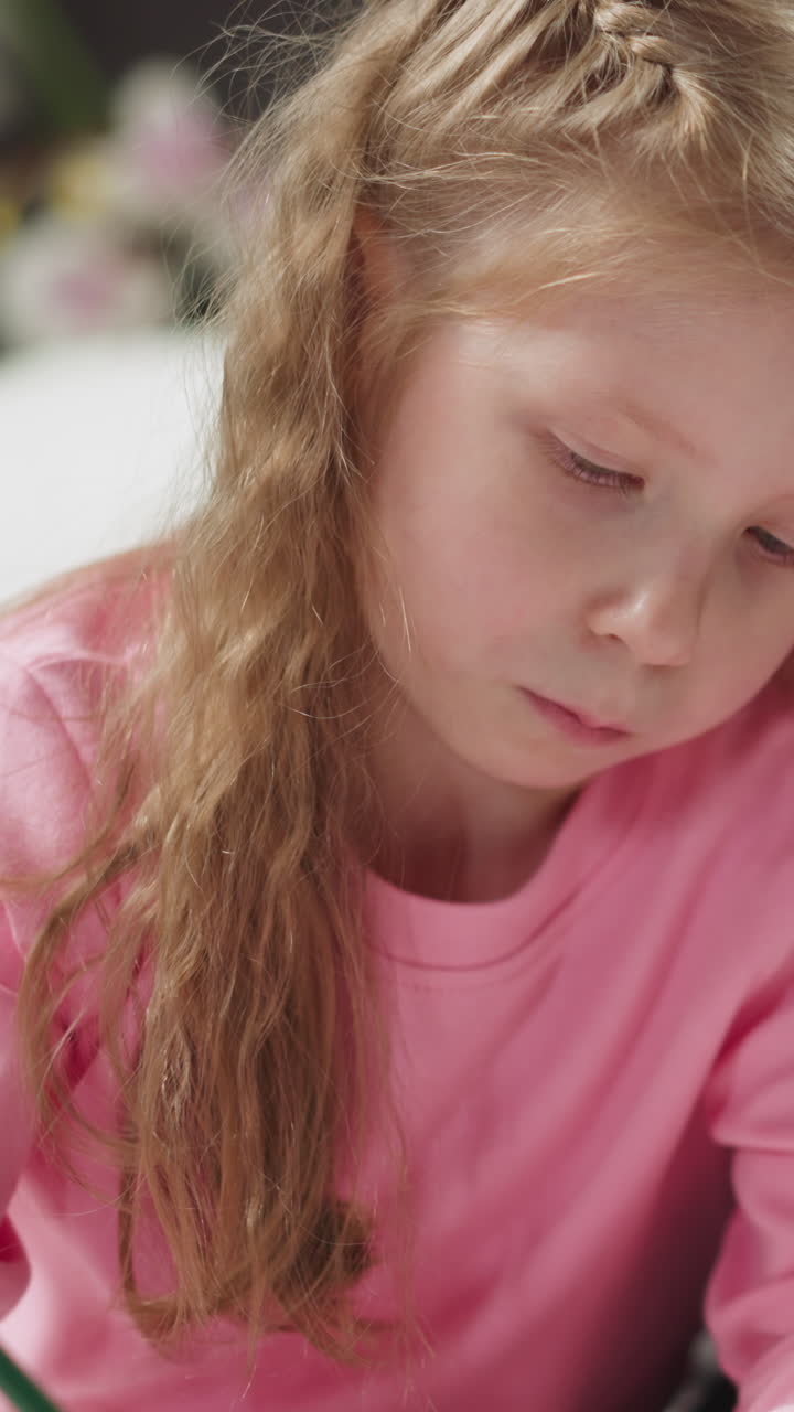 Concentrated little girl draws picture with pencil at homeschooling with African-American native speaker private teacher at home closeup slow motion
