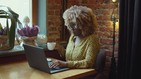 african american woman having coffee and working online in cafe