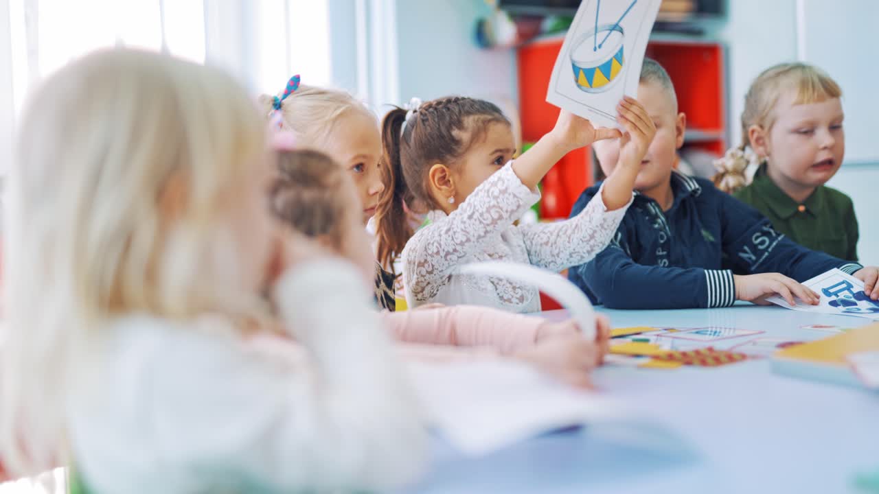 Little boys and girls study at school with pictures. Elementary school children sitting together at the table and showing the necessary pictures to their teacher.