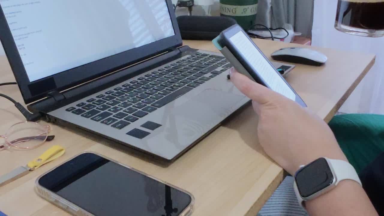 Hands using a tablet to consume information (news, reports) while simultaneously working on a laptop