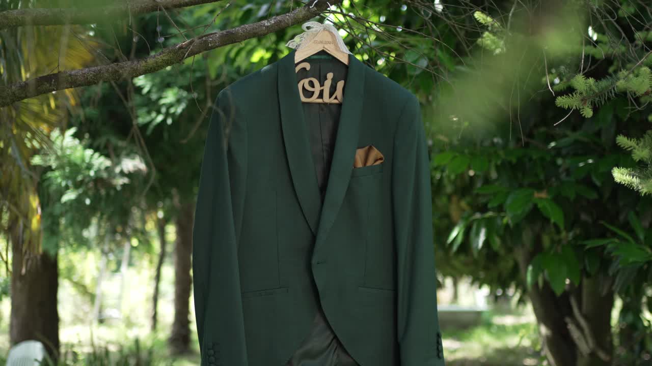 Elegant green groom’s suit with gold pocket square hanging on a tree in nature