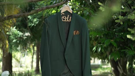 elegant green groom’s suit with gold pocket square hanging on a tree in nature